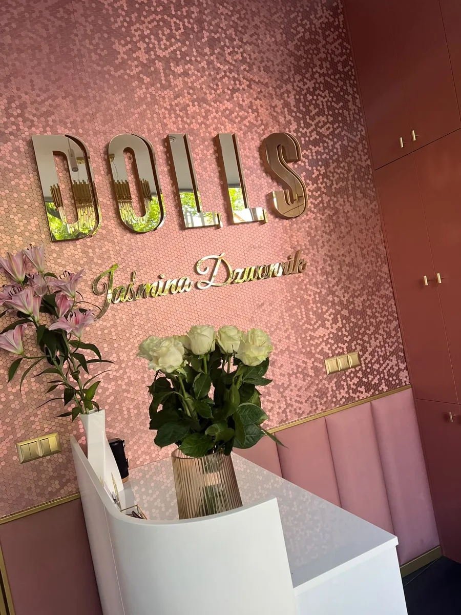 Recepcja DOLLS Studio: różowa połyskująca ściana, złoty szyld i świeże kwiaty